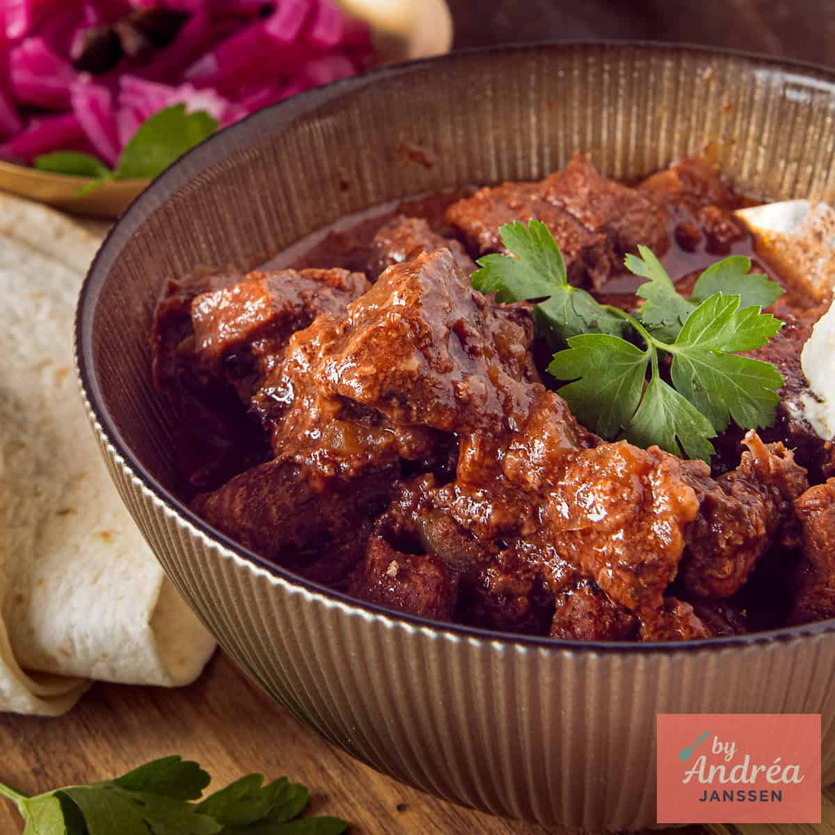 A square photo of Mexican stew in a bowl, with wraps and garnish.