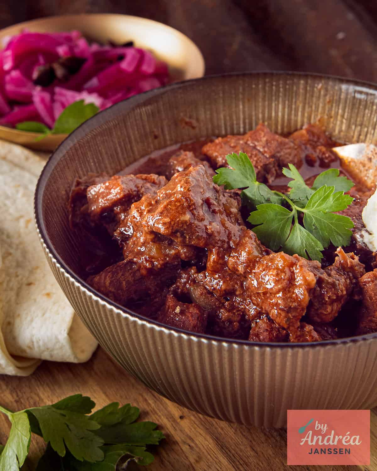 A golden bowl of carne guisada on a wooden board.