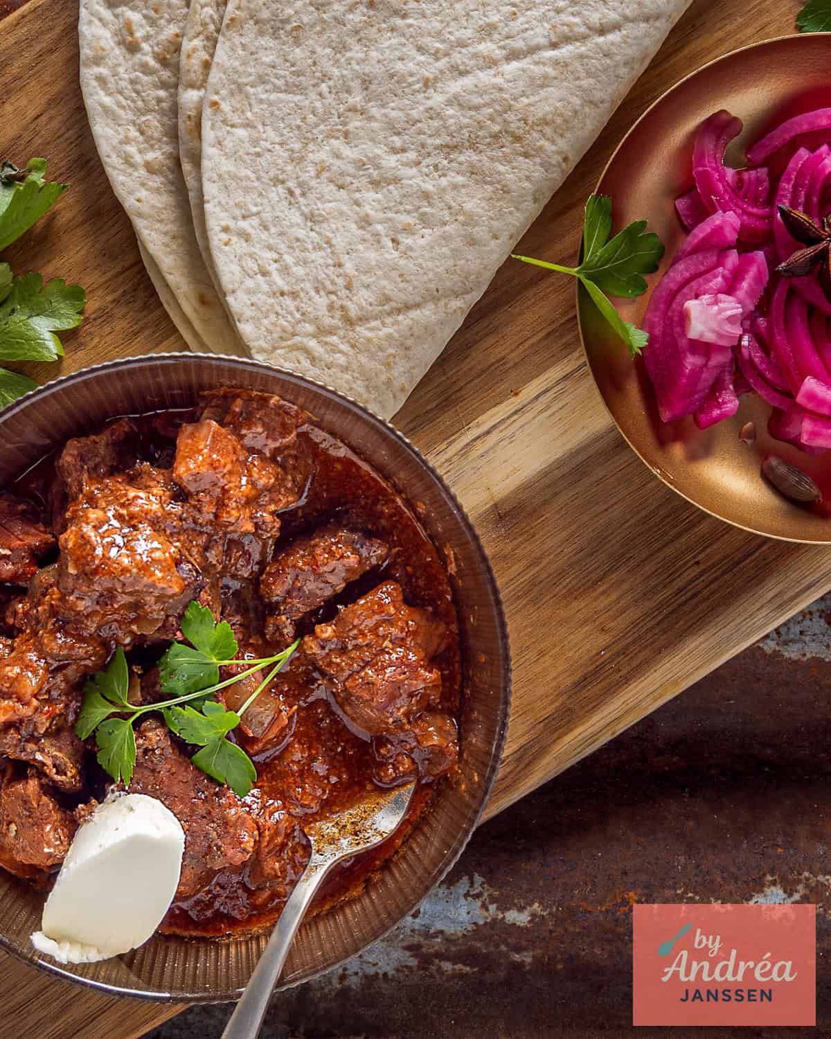 An overhead shot of a slow cooker bowl of carne guisada, wraps, and onion pickles