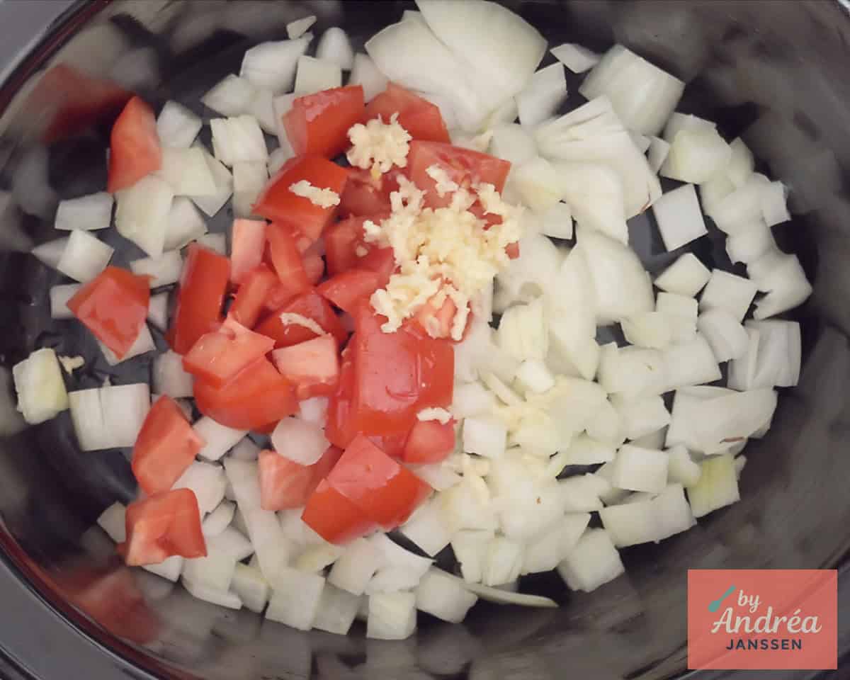 Onion, tomato and garlic in the bottom of a slow cooker.