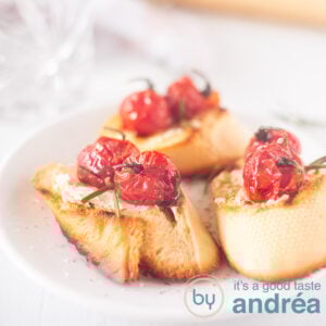 A square photo with three bruschetta topped with goat cheese and roasted tomatoes on a white background