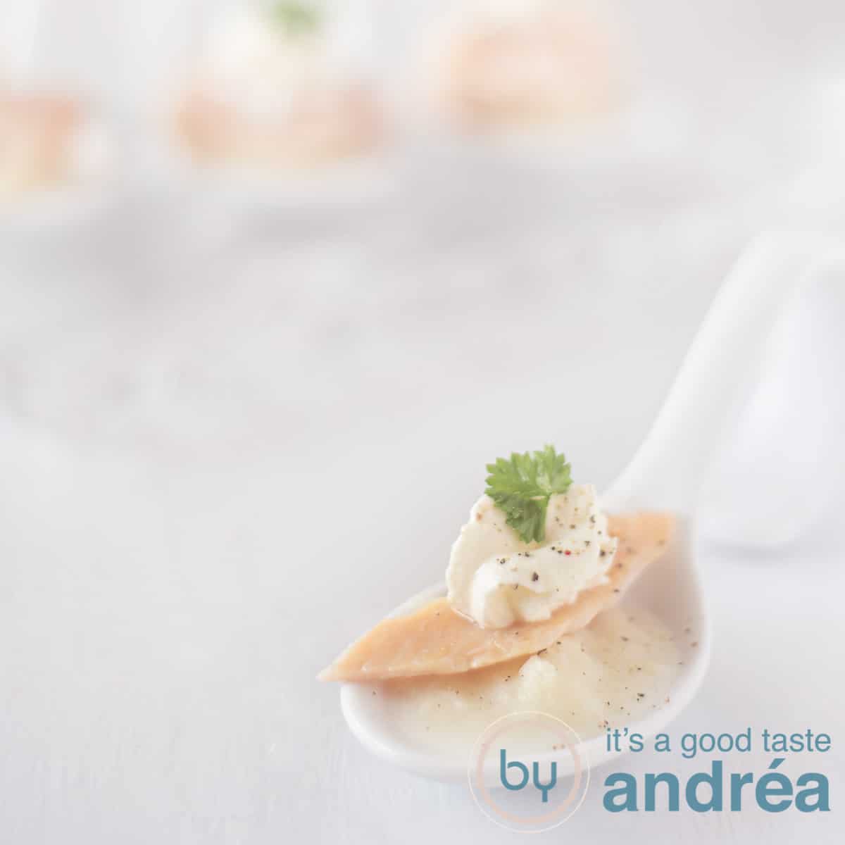 A square photo with a white spoon filled with asparagus mousse, trout and horseradish tuft on a white background in the background three more amuse spoons