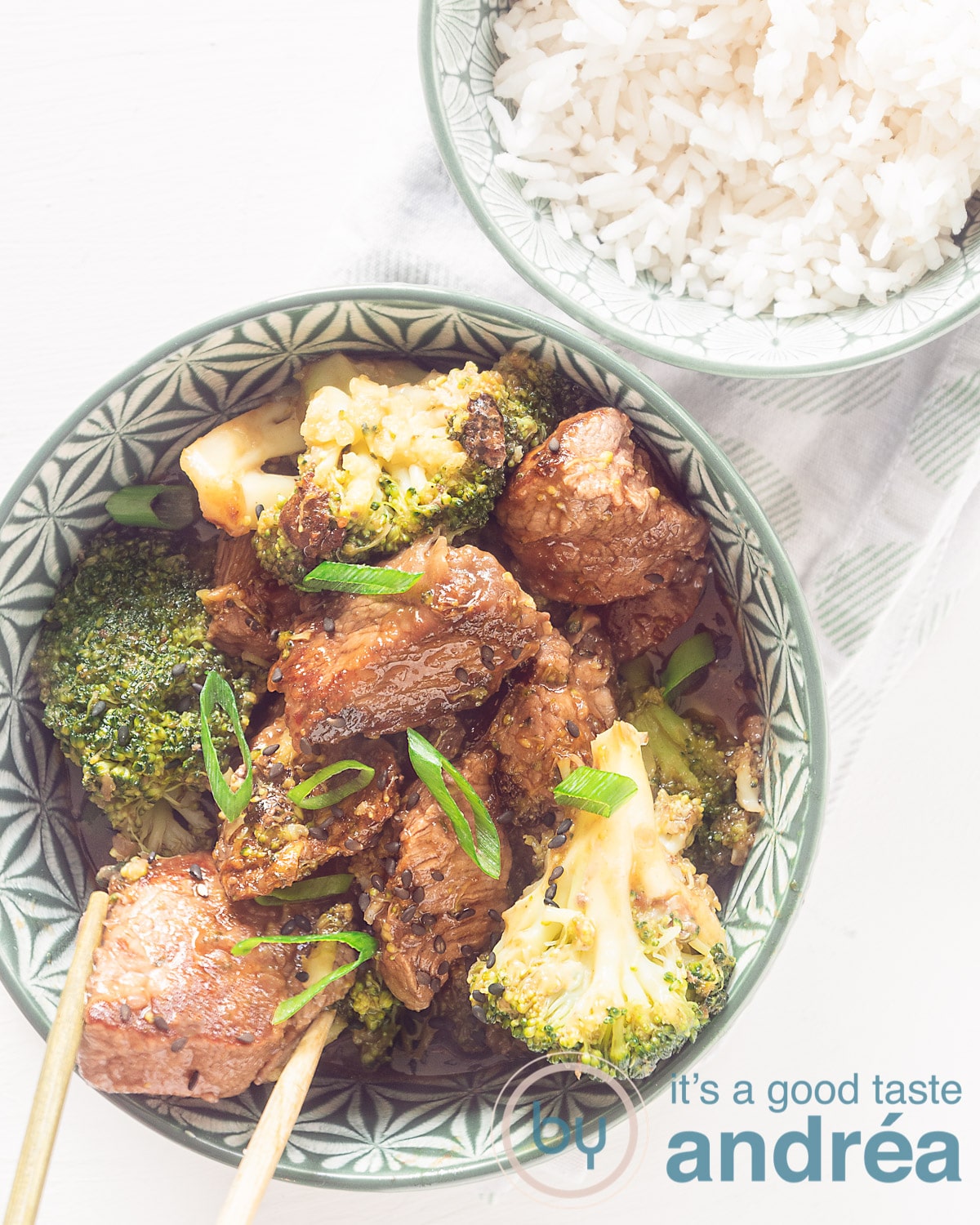 A photo from above with a bowl filled with broccoli and steak in teriyaki sauce and a bowl with rice on a white background