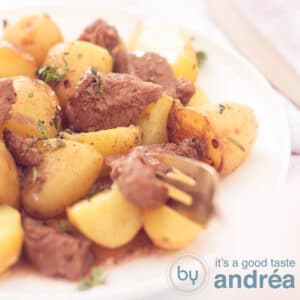 A square photo with a white plate filled with potatoes and steak. A golden fork takes a piece of steak