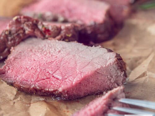 A square photo with slices of roast beef on baking paper with a piece cut off