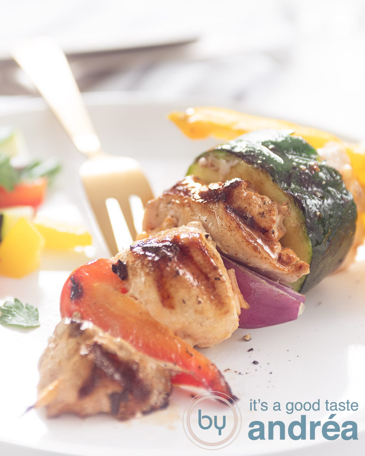 A shashlick with vegetable chicken and pork tenderloin on a white plate. A golden fork in the background