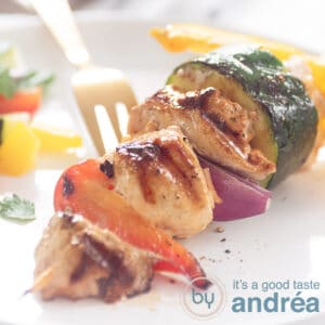 A square photo with a pork tenderloin, chicken and vegetable skewer on a white plate