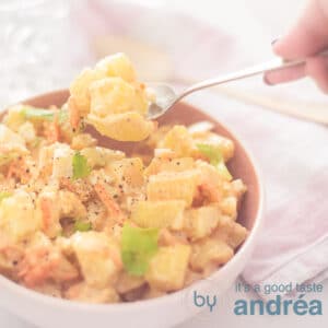 a square photo of a pink bowl filled with potato salad amish style. A spoon takes a bit out of the bowl