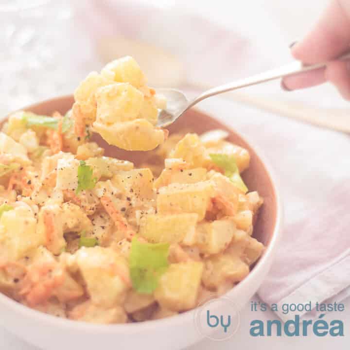a square photo of a pink bowl filled with potato salad amish style. A spoon takes a bit out of the bowl