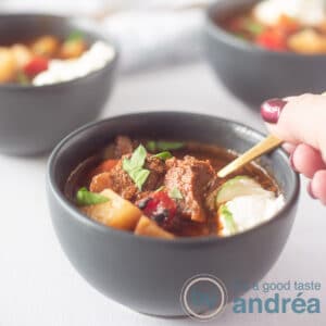 a square photo of a grey bowl filled with Hungarian Goulash soup with beef, potato and sour cream.