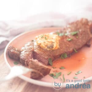 A square photo with a piece of sirloin steak with a piece cut off on a pink plate. Herb butter melts on the sirloin steak