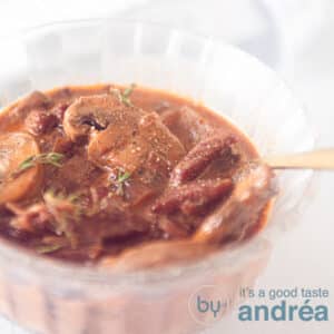 A glass dish filled with brown hunter sauce with mushrooms and thyme.