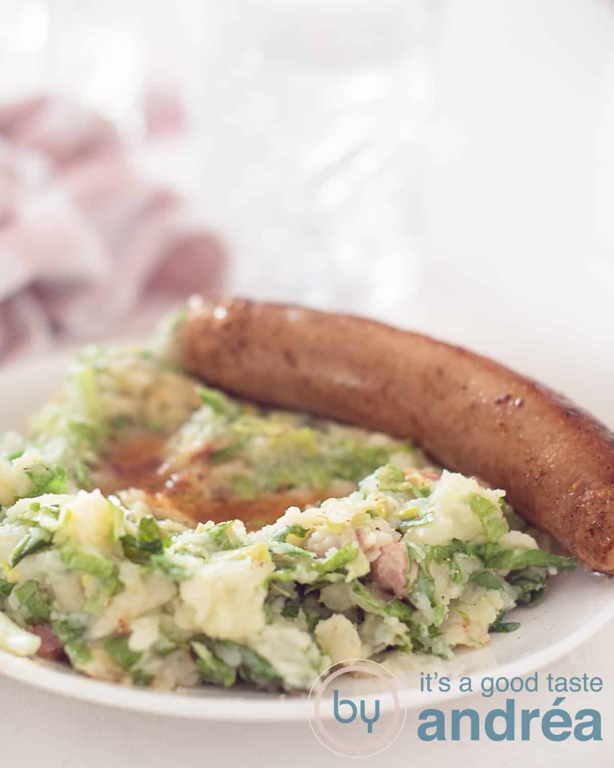 An elevation photo with a white plate with endive stew, gravy and sausage. In the background a glass and a pink white tea towel.