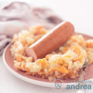 A square photo with a pink plate with stew and smoked sausage.