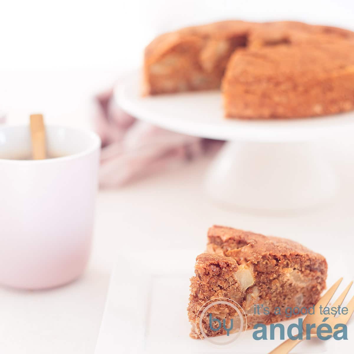A square photo with a piece of pear cake in the foreground and in the background a cake stand with the rest of the cake. On the left a pink cup with coffee.