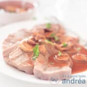 A square photo with a white dish with strips of beef tongue and Madeira sauce. In the background a bowl with extra sauce on a white background