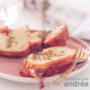 A square photograph showing part of a pink plate with chicken roulade slices on top and a white background