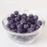 A glass bowl with fresh blueberries on a white background