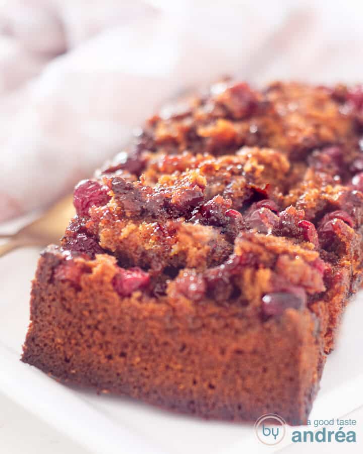 Op een wit schaaltje ligt een cake met cranberry topping en twee kopjes met koffie