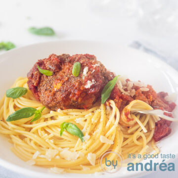 A square photo with a white deep plate filled with spaghetti tomato sauce and tasty meatballs with sage and Parmesan cheese. A white background.