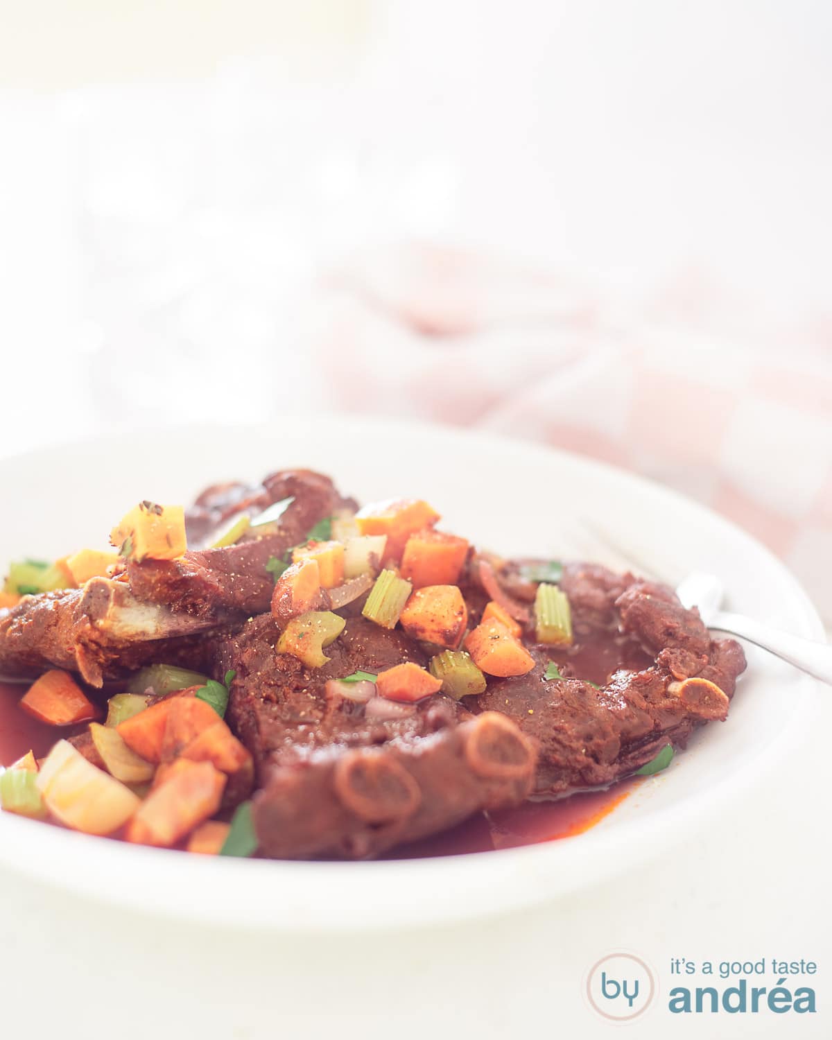 braised ribs in red wine on a white plate on a white background. The ribs are covered with veggies.