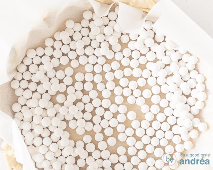 A quiche dish with dough, baking paper and filled with baking beans.