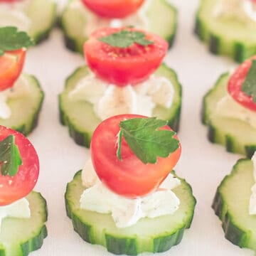 a plate with cucumber slices topped with herb cream cheese and a half cherry tomato