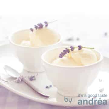 Two white bowls with lavender ice cream, a sprig on top. On a white dish with a spoon on the left. Standing on a checkered tablecloth