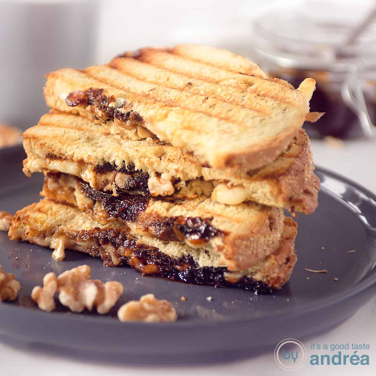 A square photo with a gray plate with a stack of toasted sandwiches with Camembert and walnuts in front.