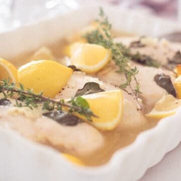 a white casserole with chicken, lemon and thyme. A blue bowl and white cloth