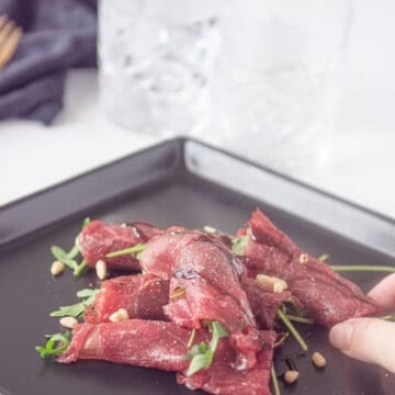 Beef carpaccio roll on a black plate