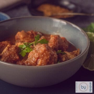 A square photo with a pink bowl filled with chicken curry with coconut and delicious herbs. A white background.
