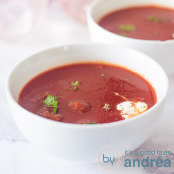 A square photo of two bowls of tomato, cream and parsley soup