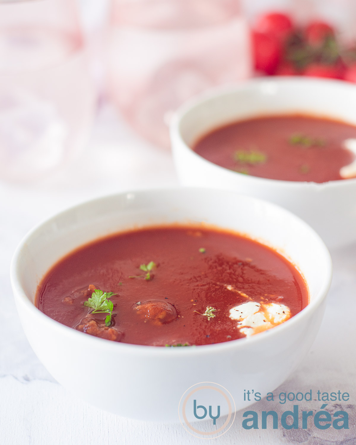 Two bowls of tomato soup with meatballs, cream, and fresh parsley. Two spoons in the background.