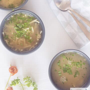 a bowl with noodle soup with herbs and a slice of bread