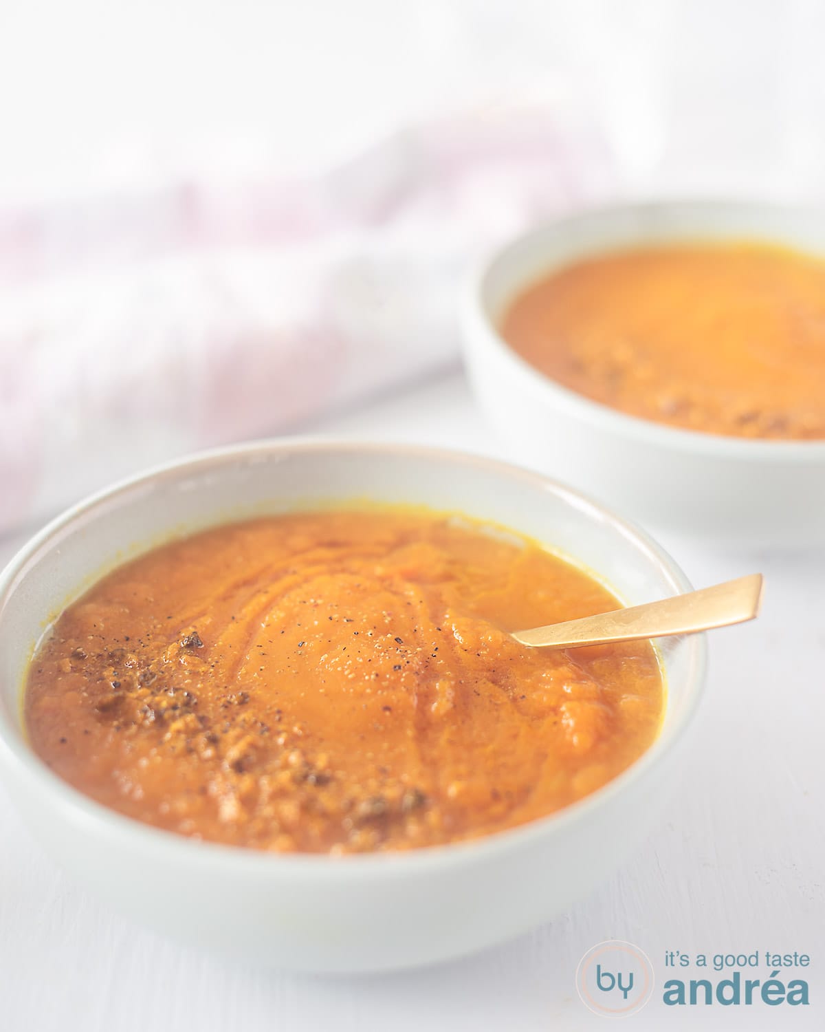Two blue bowls with curry carrot soup in a diagonal.