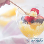 a square photo with part of a glass filled with orange beer sorbet and topped with fresh fruit. A golden spoon