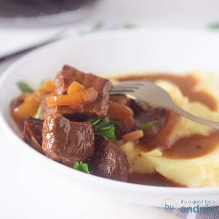 A square photo showing part of a deep white plate of mashed potatoes and hash. On a white background