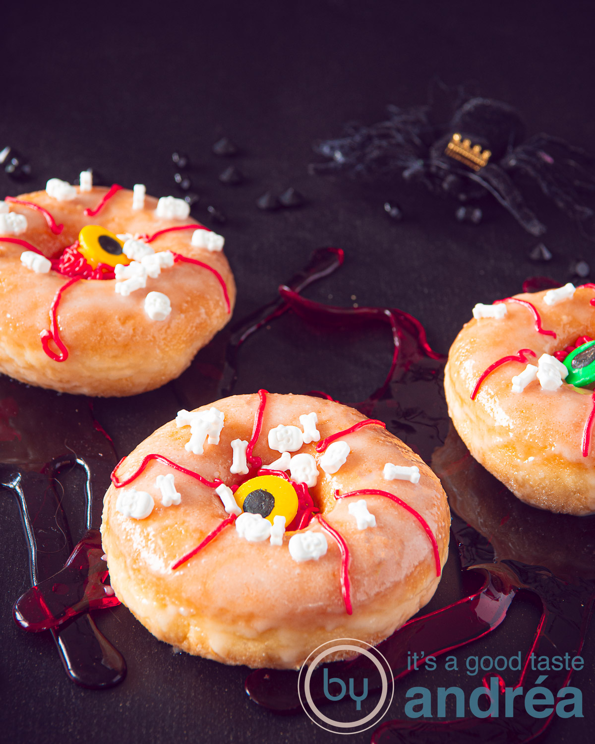Three Halloween donuts with eyes and red blood stripes on a black background