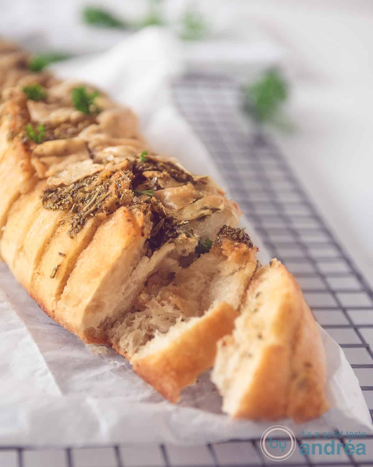 A baguette with herbs and garlic on a baking paper. Two slices are cut of the baguette