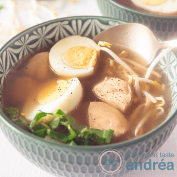 A square photo of a green bowl filled with Japanese noodle soup with chicken, bok choy, bean sprouts and eggs. A golden spoon takes a bite.