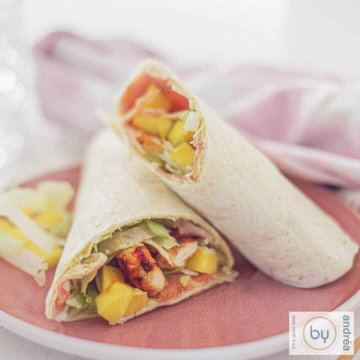Een vierkante foto met een roze bord met twee halve Wraps met mango en kip