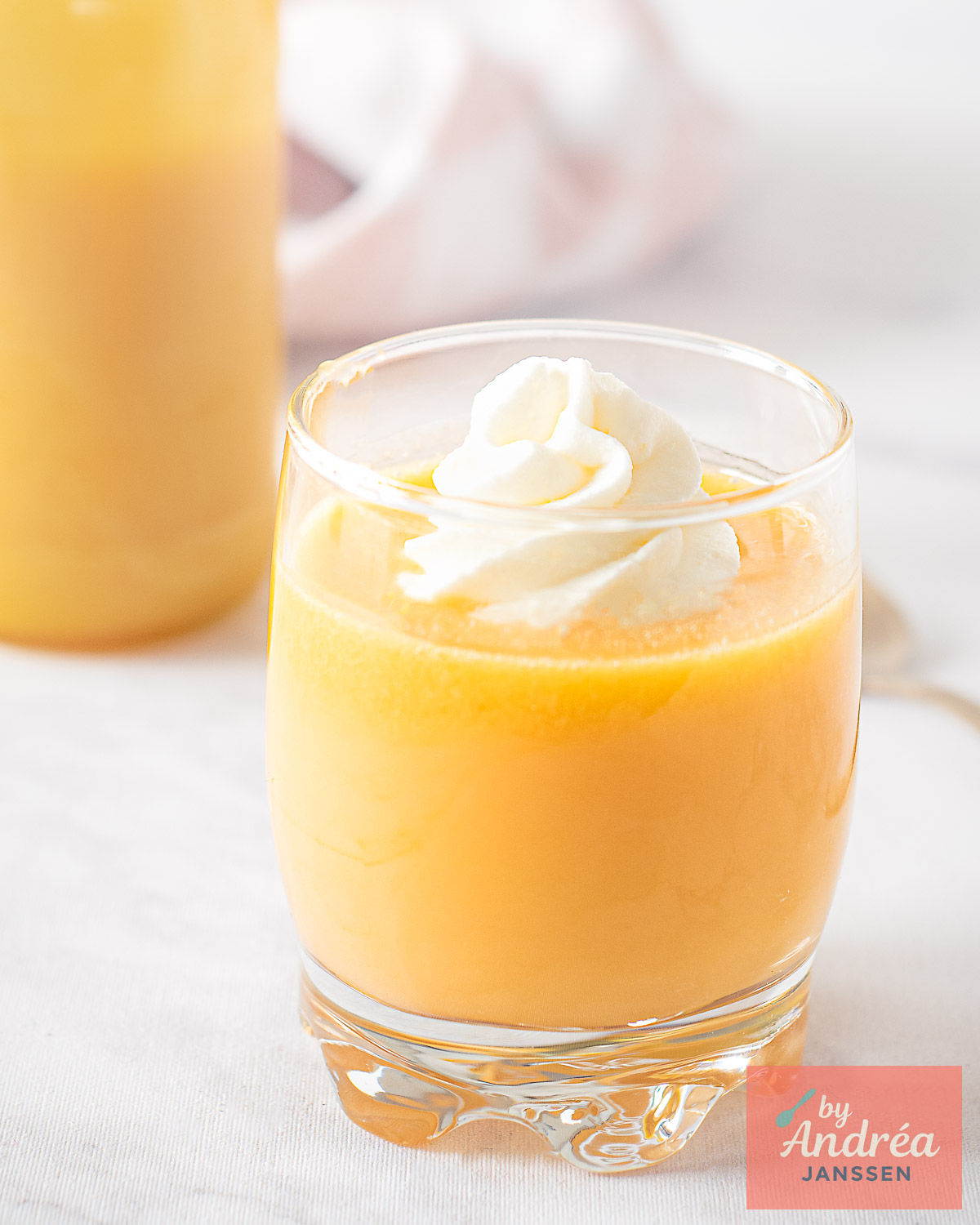 Glass of Dutch advocaat topped with whipped cream, bottle in the background