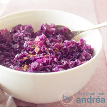 A square photo of a white bowl almost completely filled with red cabbage with apples and balsamic vinegar. A pink background.
