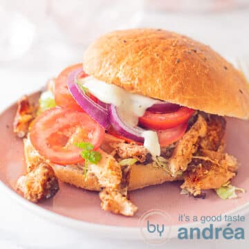 A Turkish sandwich with Döner chicken, tomato and lettuce and garlic sauce. A pink plate and a white background.