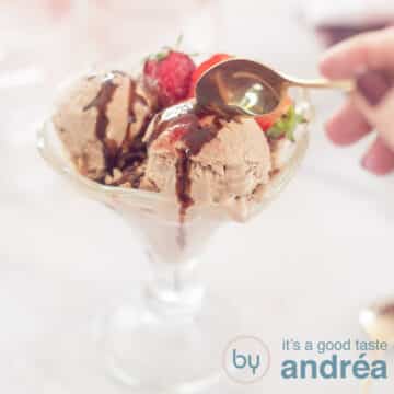 A square photo with a coupe with three scoops of chocolate yogurt ice cream, strawberries and chocolate sauce. A golden spoon takes a bite.