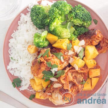 A square photo with a pink plate with drumsticks, bacon, mango, sauce, slivered almonds, rice and broccoli