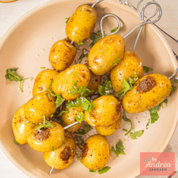 Overhead view of seasoned grilled baby potato skewers served with coarse sea salt and chopped herbs.