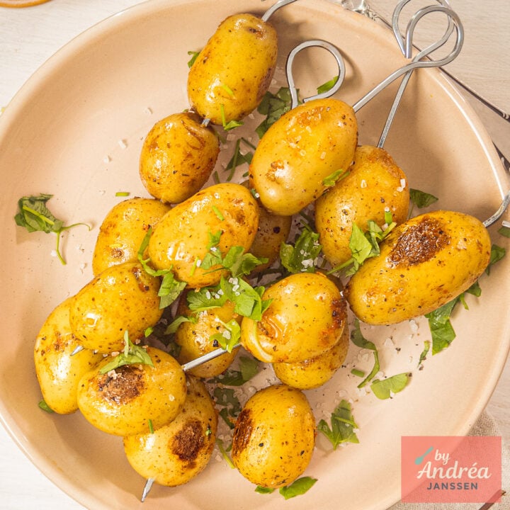 Overhead view of seasoned grilled baby potato skewers served with coarse sea salt and chopped herbs.
