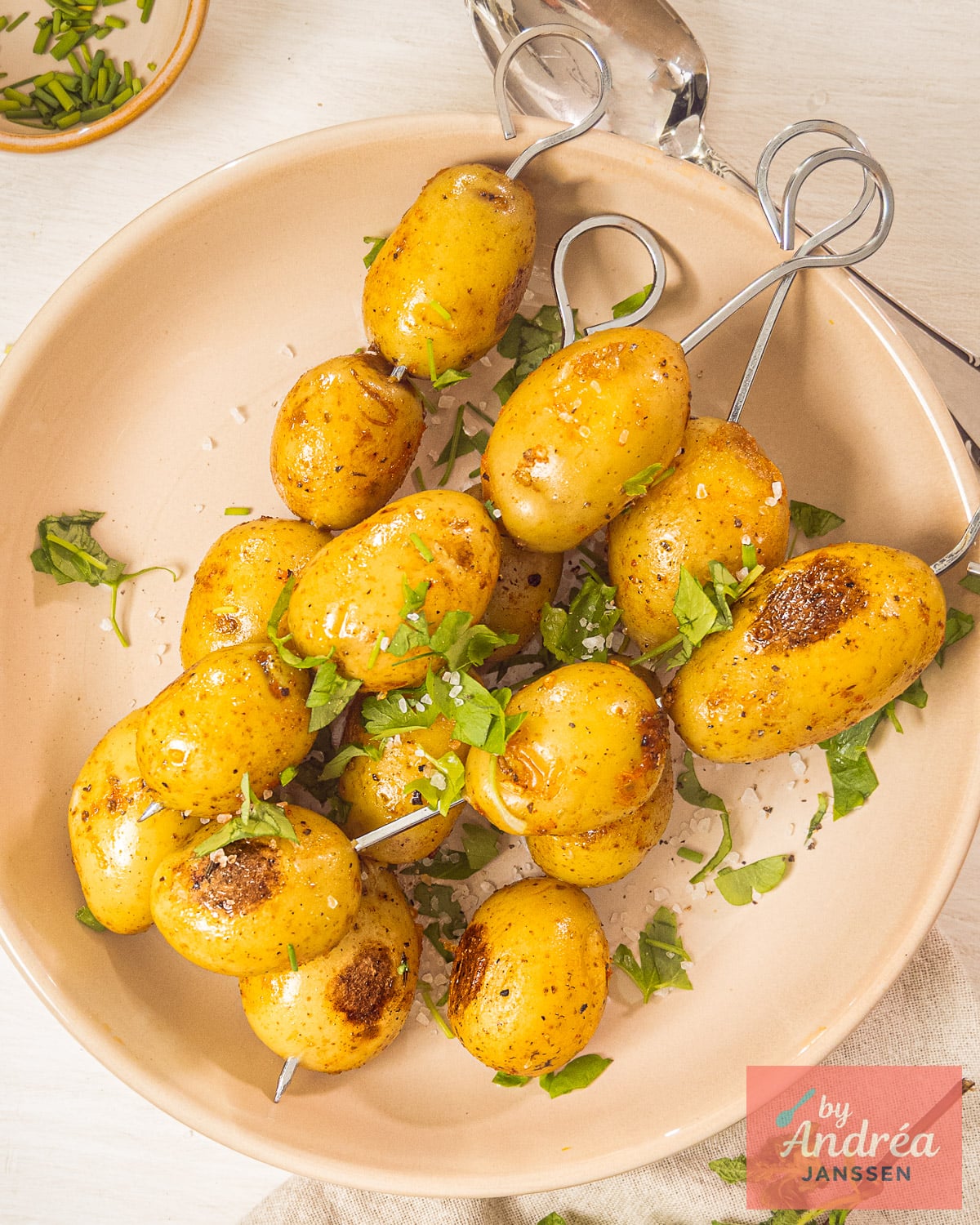BBQ baby potatoes with crispy golden edges on metal skewers, served on a large beige plate.